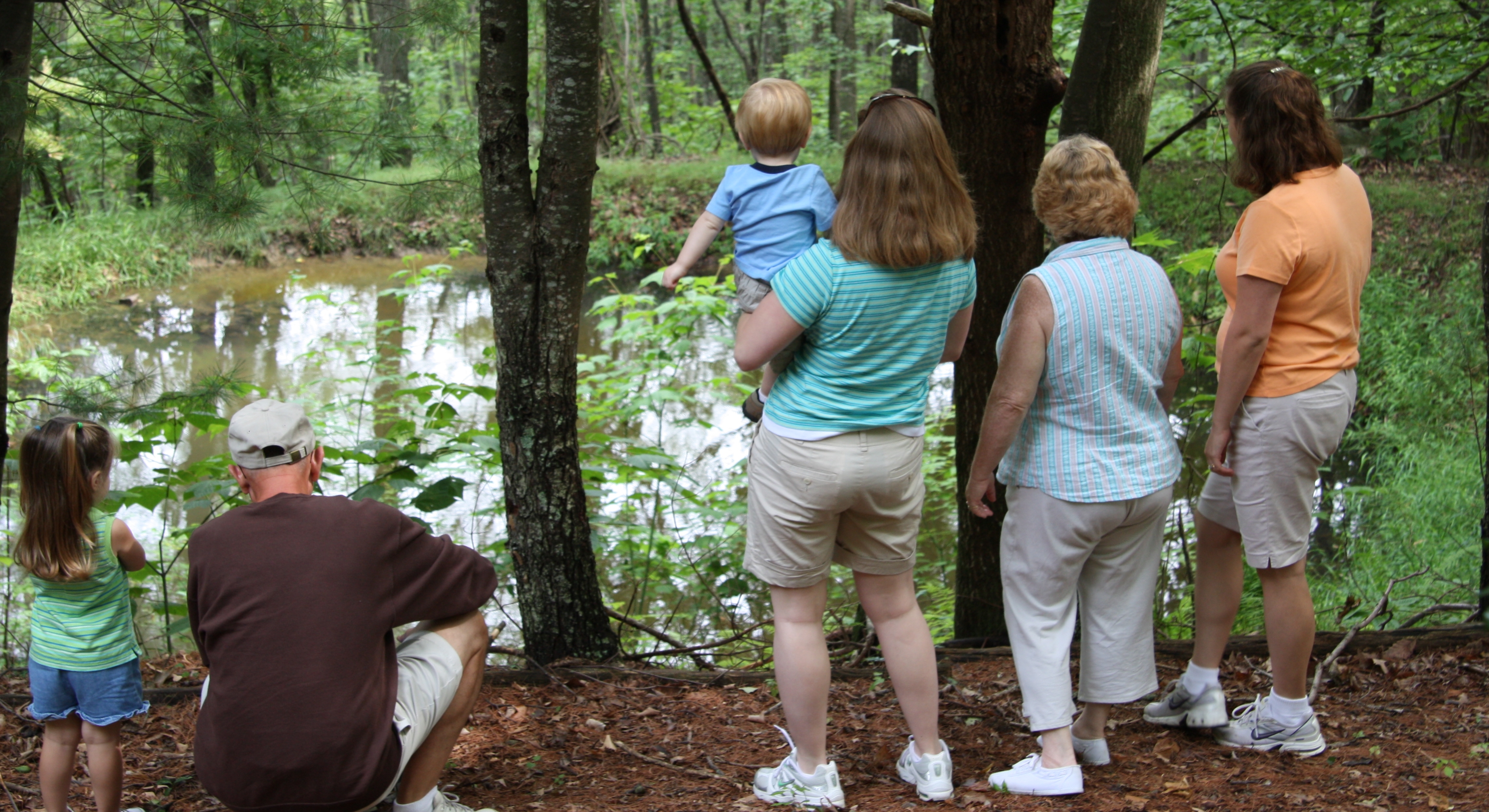 A multi-generational family look at a pond in their woods.
